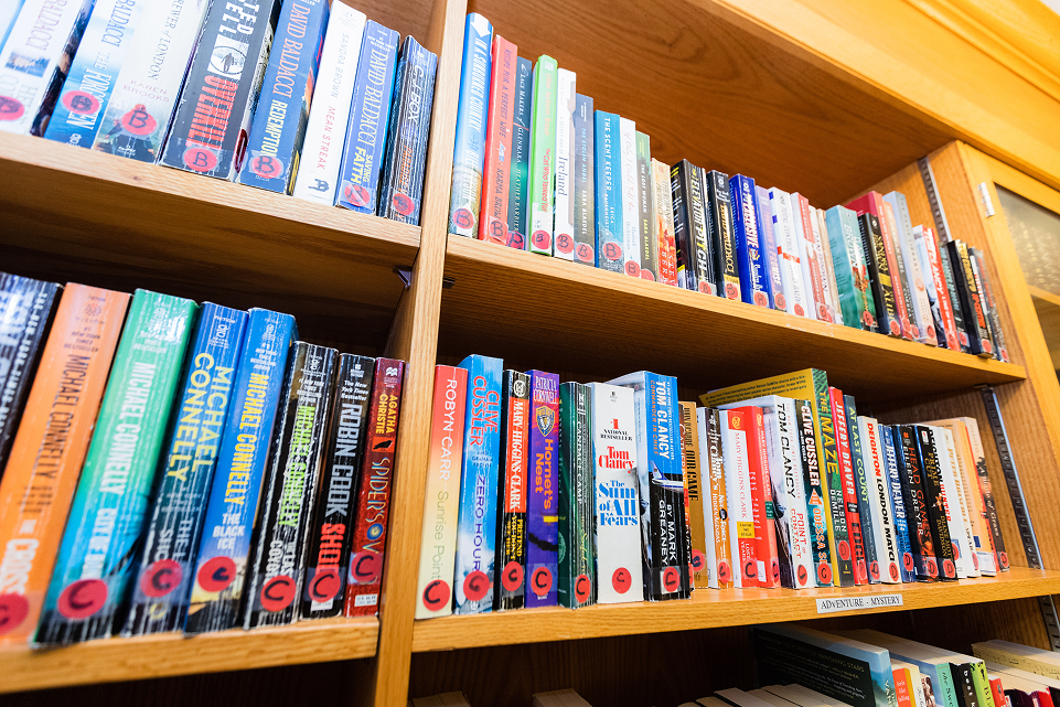 Wooden bookshelf filled with various mystery and adventure novels, many with red circular library labels.