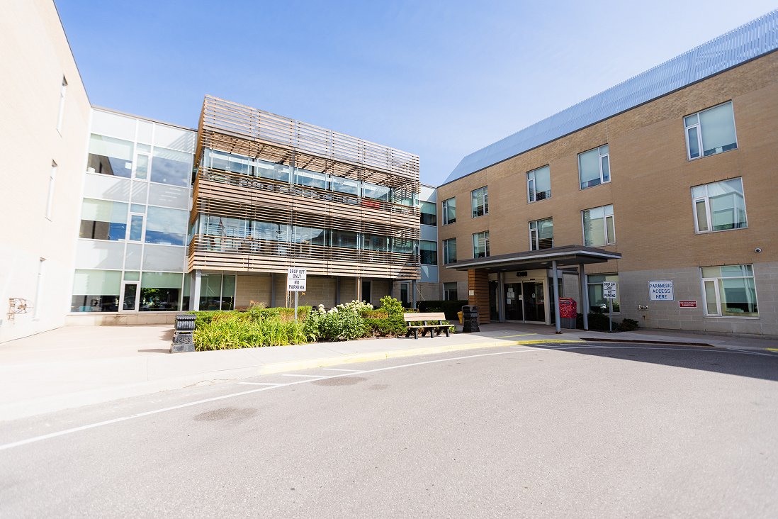 Modern building with glass windows, wooden slats facade, a bench, and signs indicating visitor parking and paramedic access under a clear blue sky.