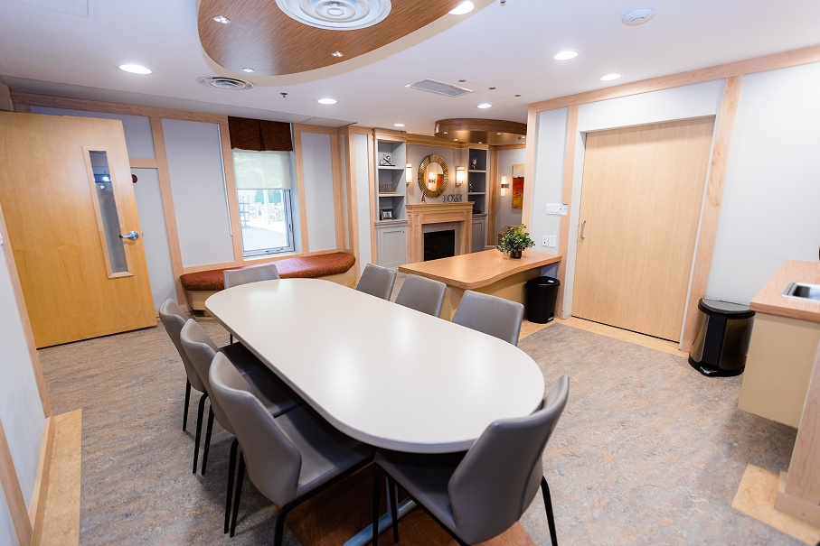 Modern conference room with an oval white table surrounded by gray chairs, wooden doors, built-in shelves, and a decorative mirror above a fireplace.