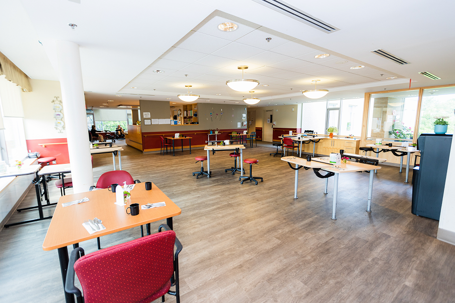 Bright dining area with spaced wooden tables and red chairs in a communal room.