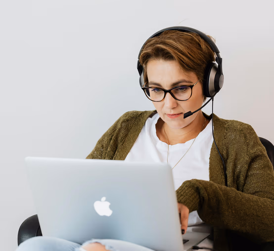 Vrouw met bril en headset werkt geconcentreerd op een laptop.