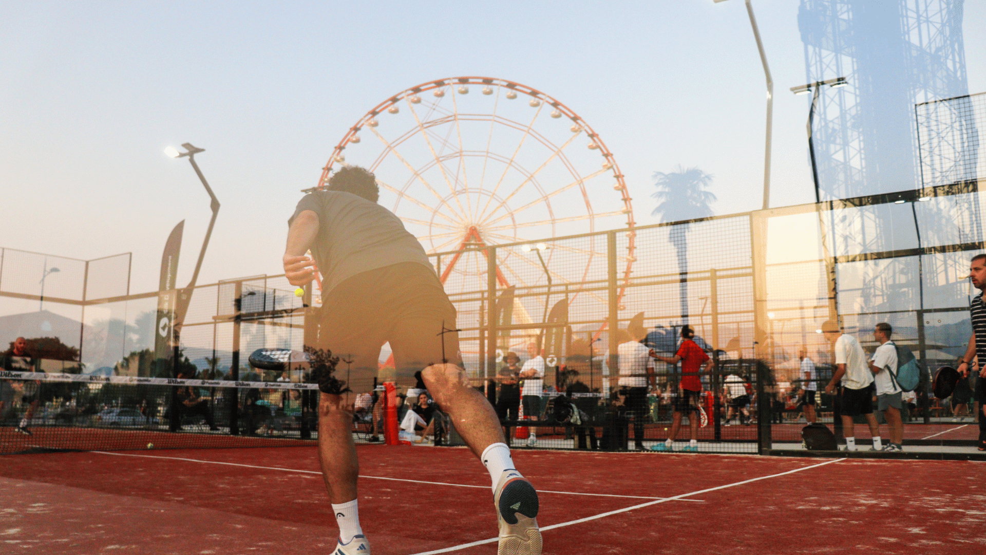 Padel Port - located in georgia, batumi. A guy playing padel on a red court, in the glass there is a reflection of a panoramic wheel. 
