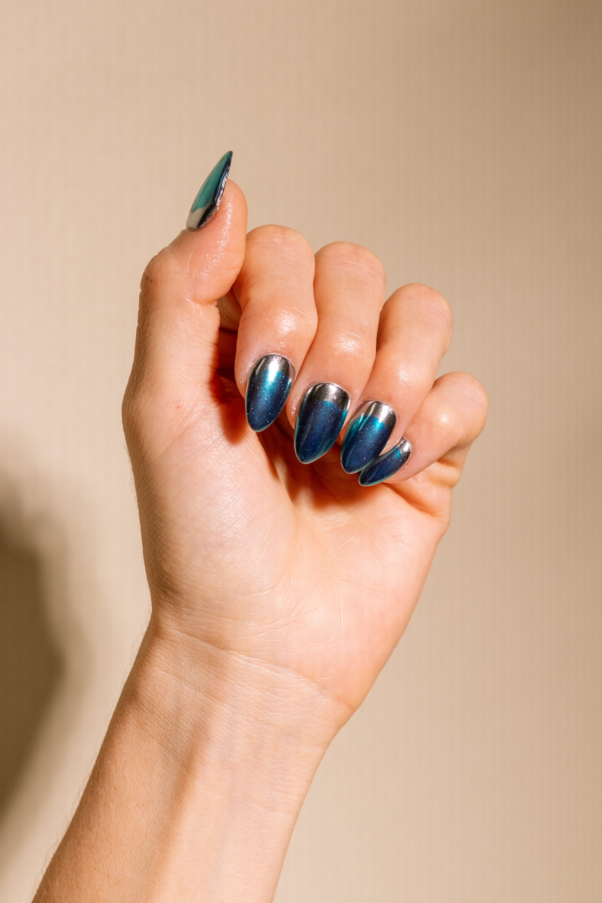 Primer plano de uñas soft gel almendradas con efecto cat eye azul y detalle metálico en la base.