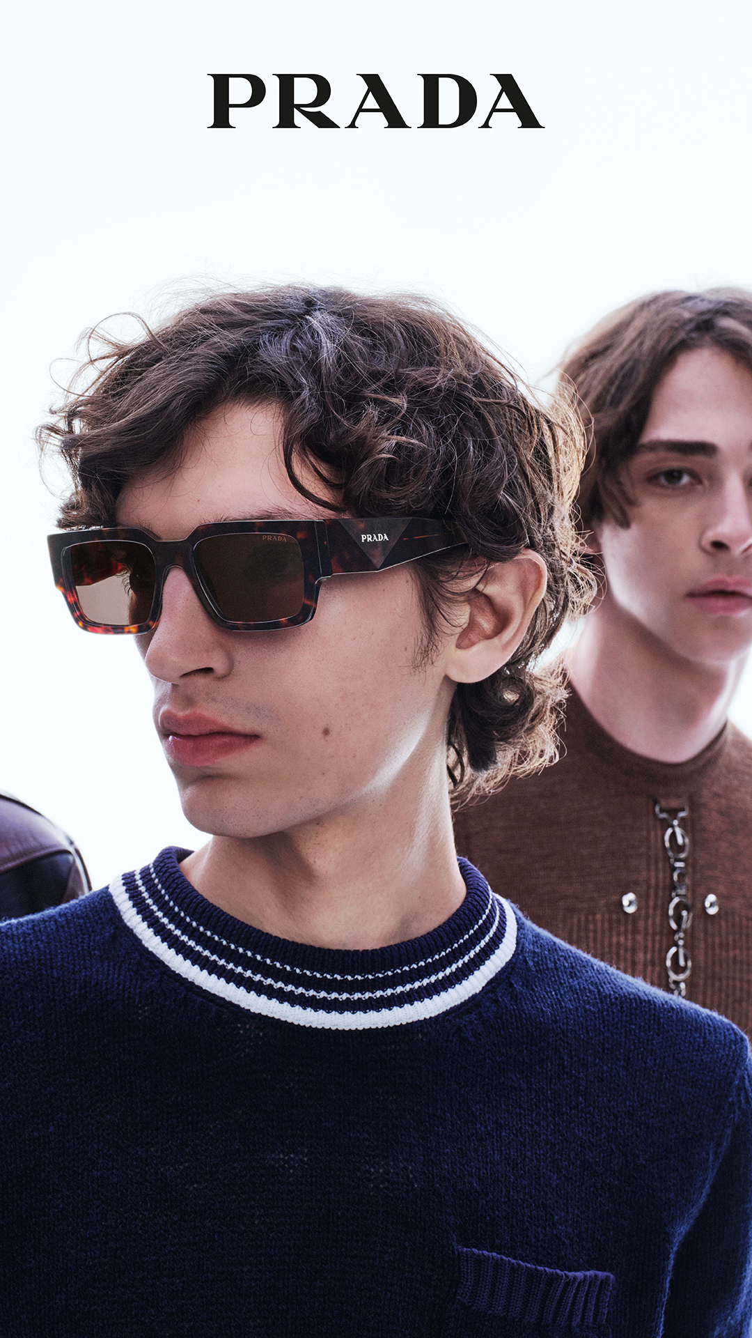 Man wearing Prada tortoiseshell sunglasses and striped sweater with two models
