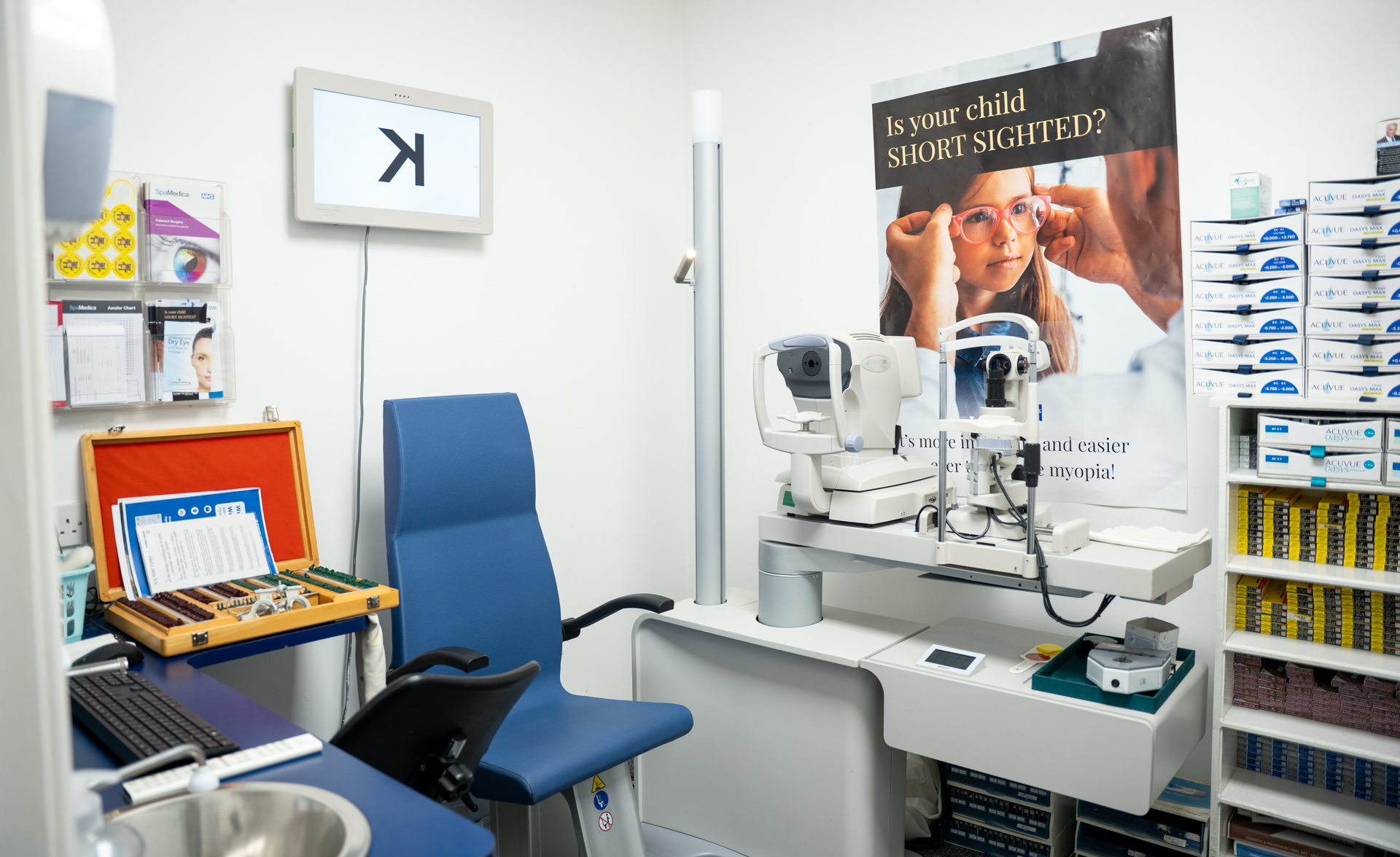 Modern optometry office with eye examination equipment, blue chair, and shelves of eyewear supplies.
