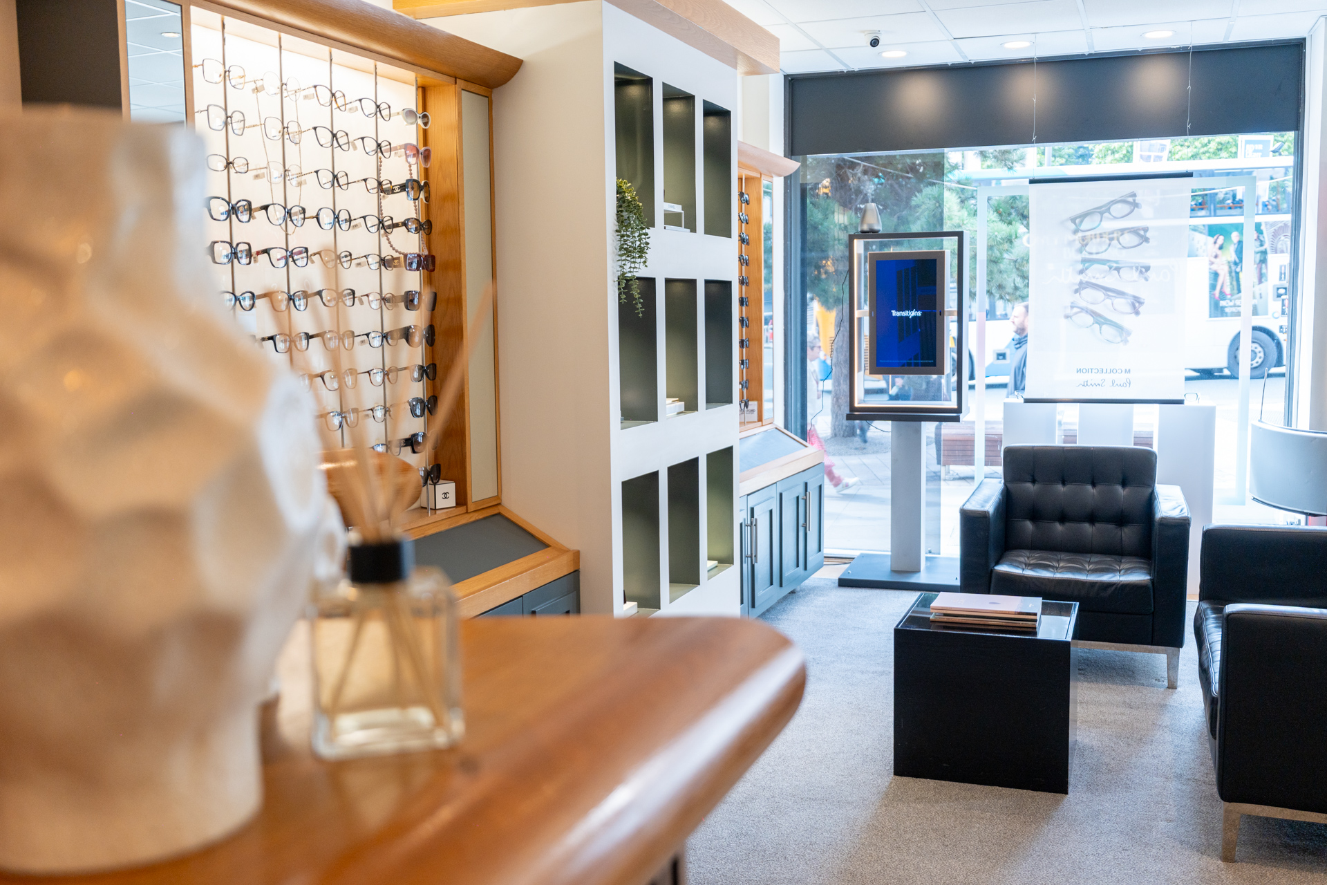 Modern eyeglass store interior with display wall, seating area, and storefront windows