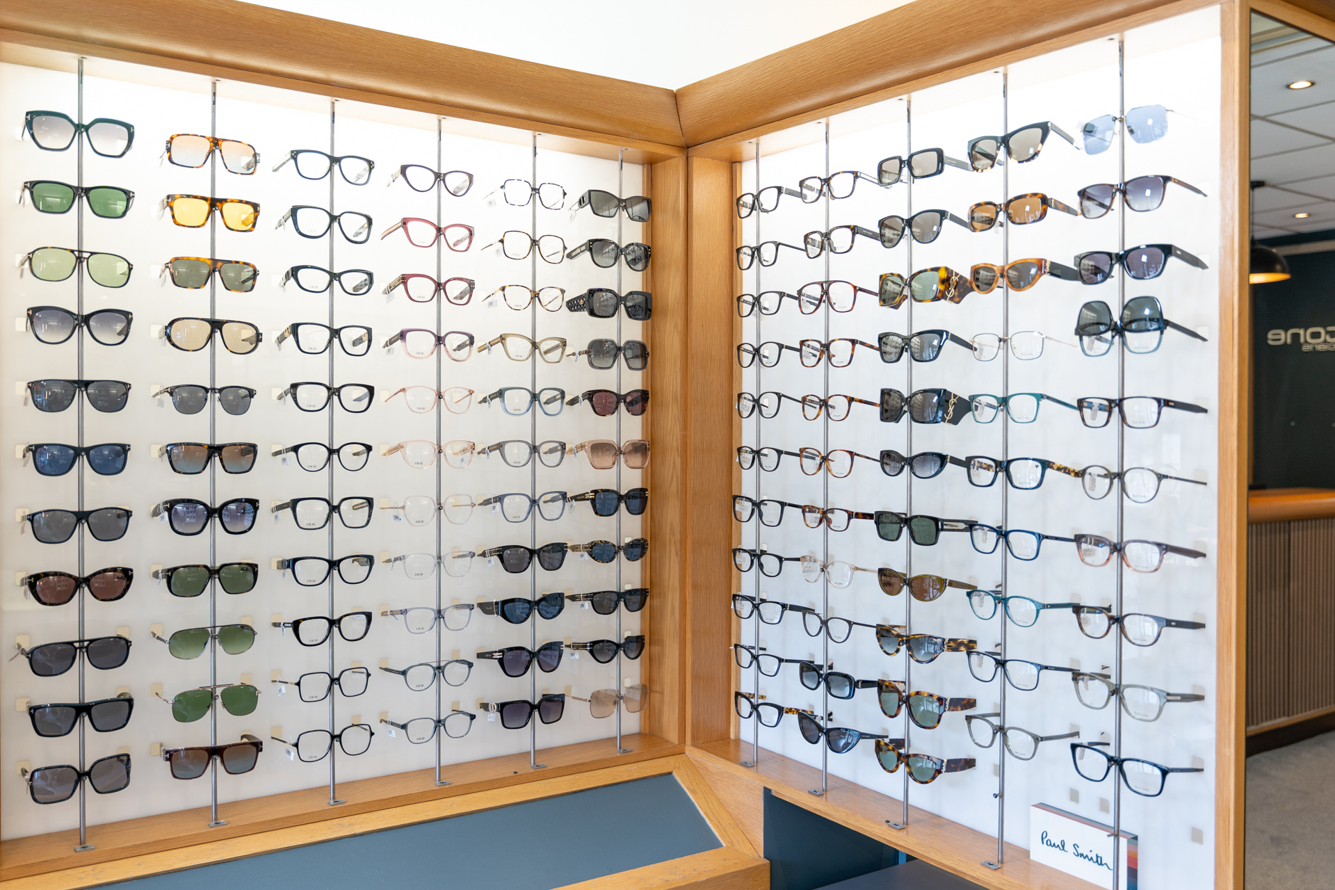 Eyeglass display case with dozens of sunglasses and optical frames organized on glass panels