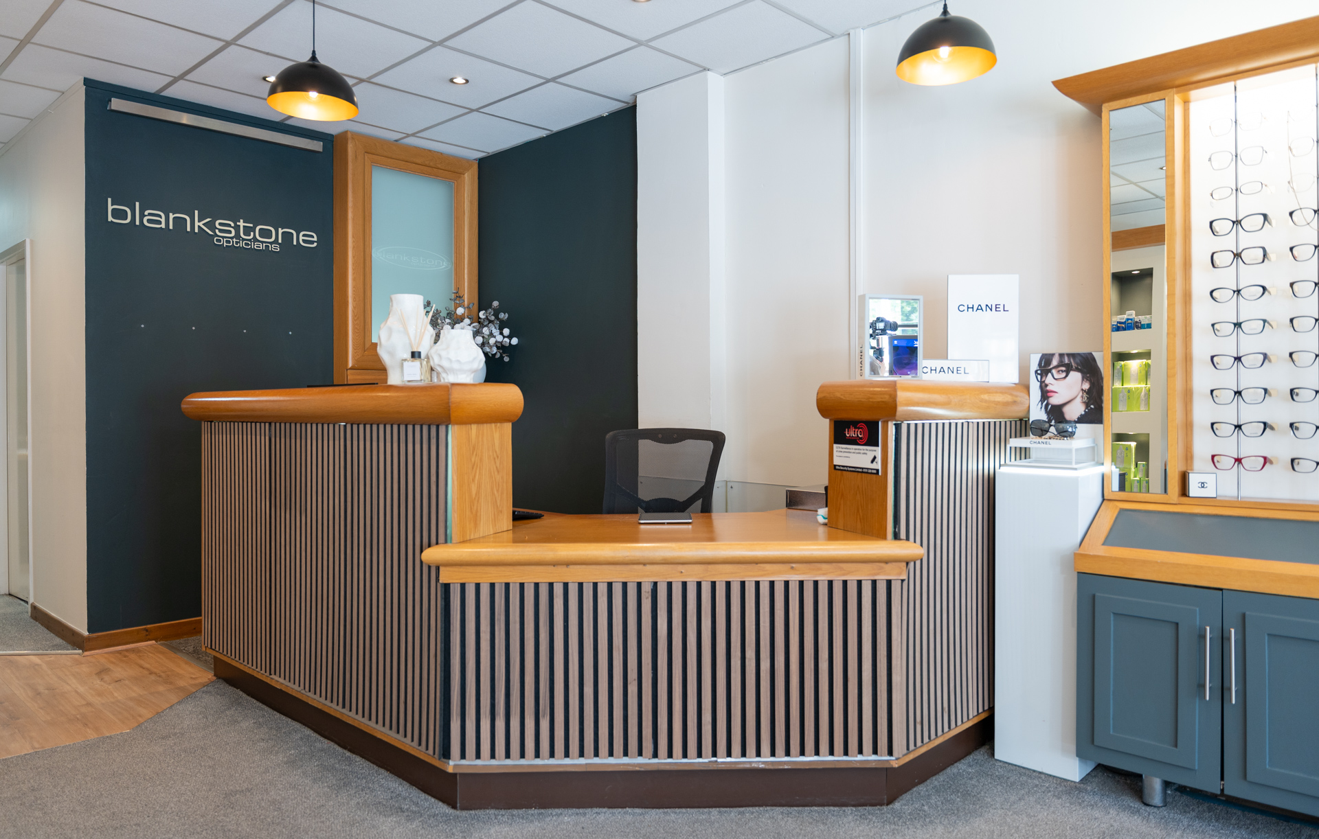 Modern optician reception area with wooden desk, dark accent wall, and eyewear display