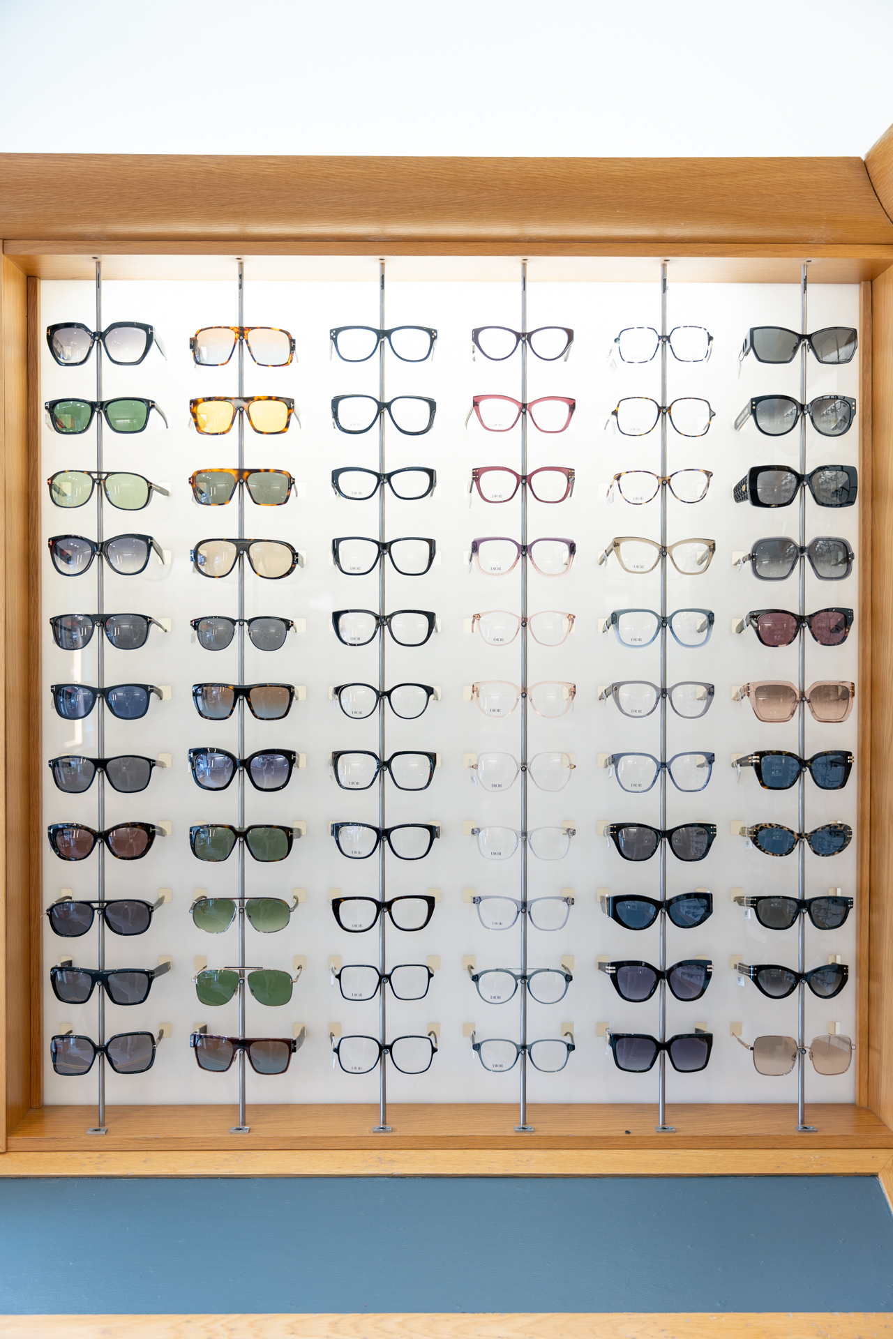Large wooden display case showing organized collection of various eyeglasses and sunglasses styles