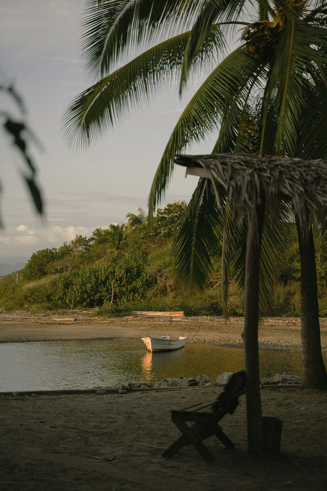 Plage tropicale au coucher du soleil avec palmiers, cabane en bois et une petite barque blanche sur l’eau calme. Paysage romantique et intimiste, idéal pour un voyage de noces ou une lune de miel sur mesure avec Beaux Périples