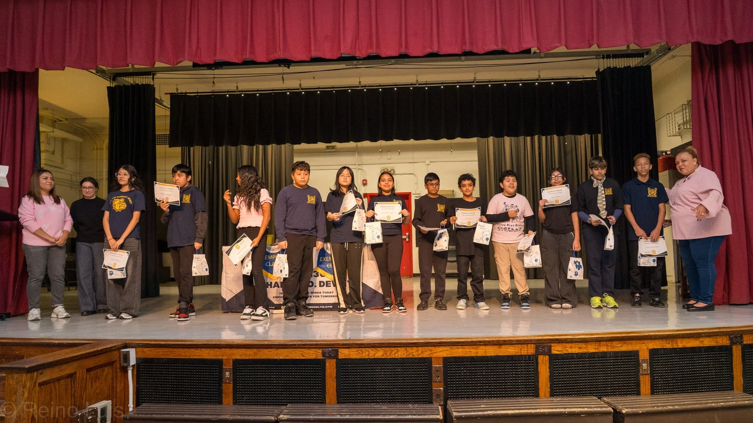 Students holding certificates and award bags on school auditorium stage