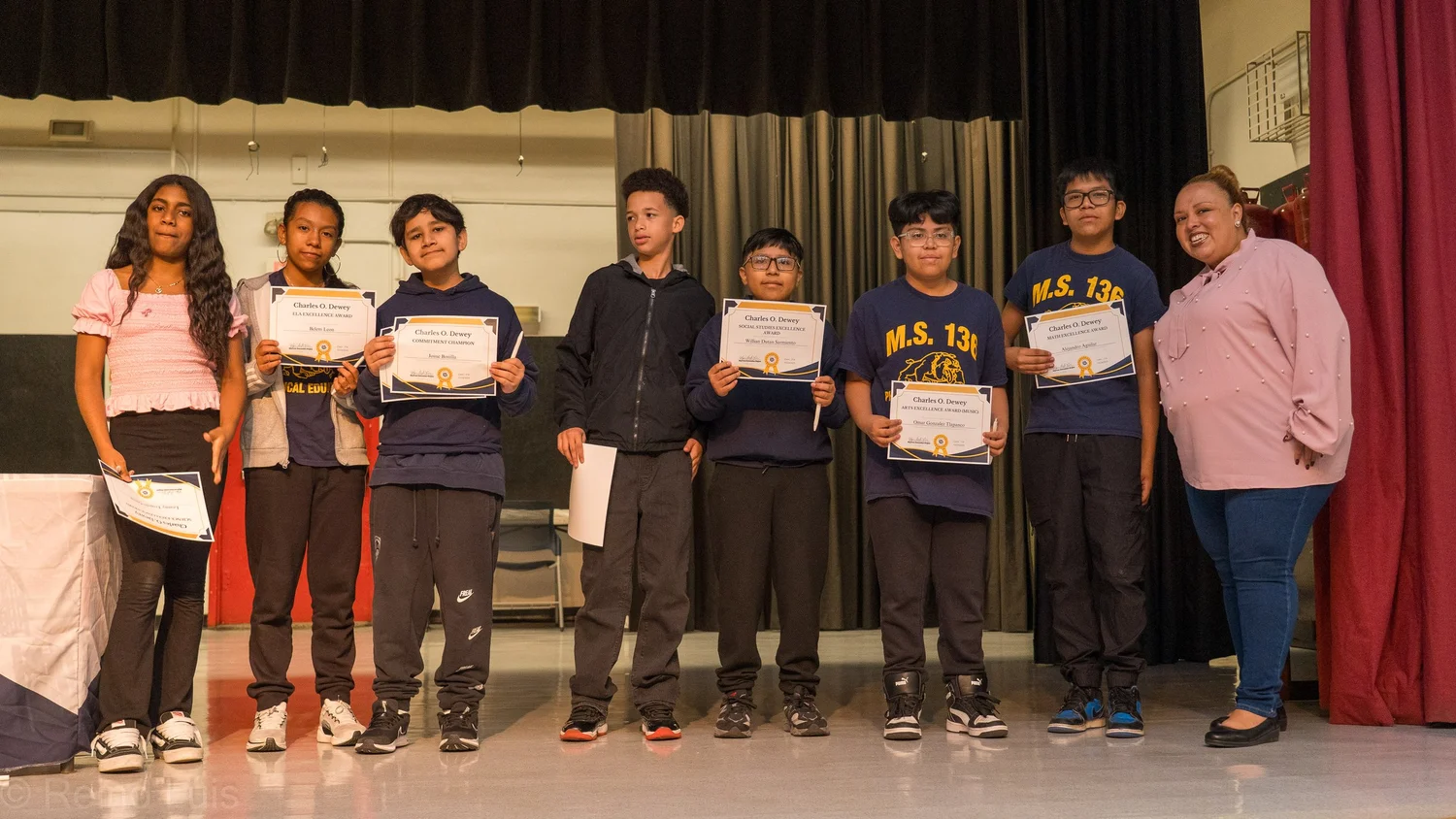 Students holding Charles O. Dewey award certificates on stage with adult presenter