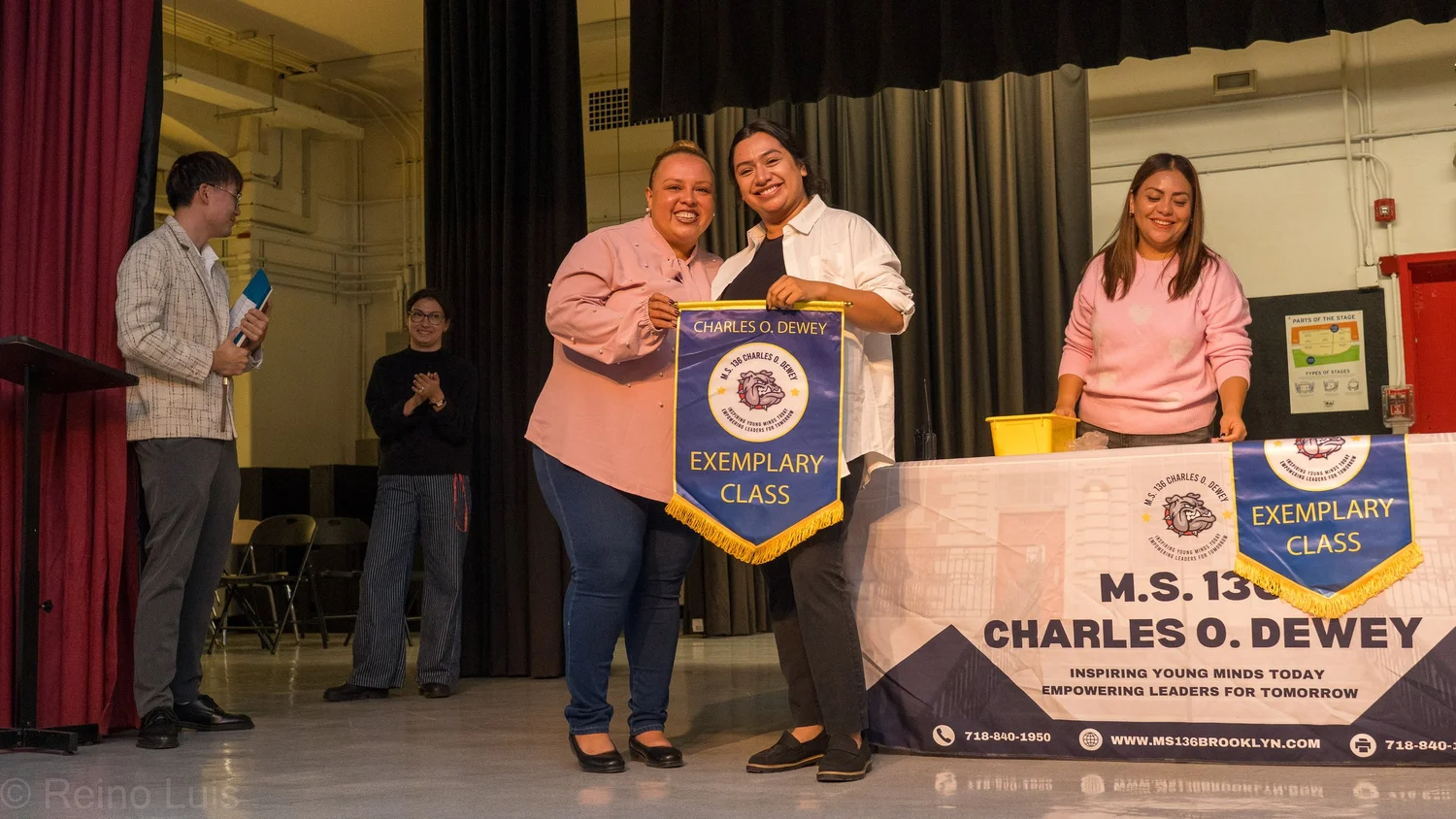Two staff members hold Charles O. Dewey Exemplary Class banner on stage