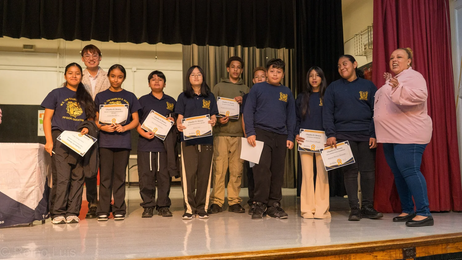 Students holding certificates on stage at a school award ceremony