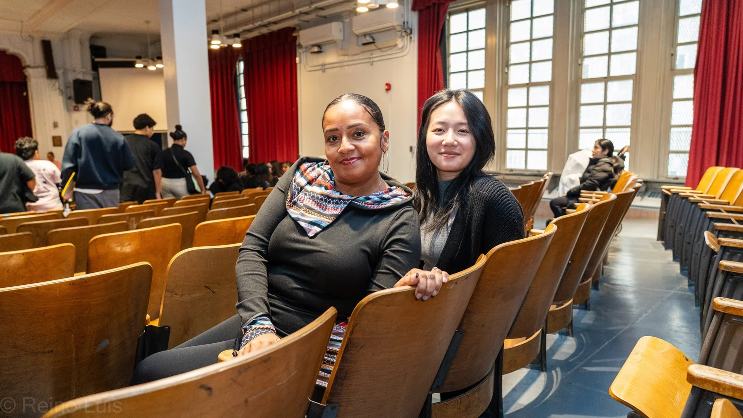 Two adults seated together smiling in school auditorium during award ceremony