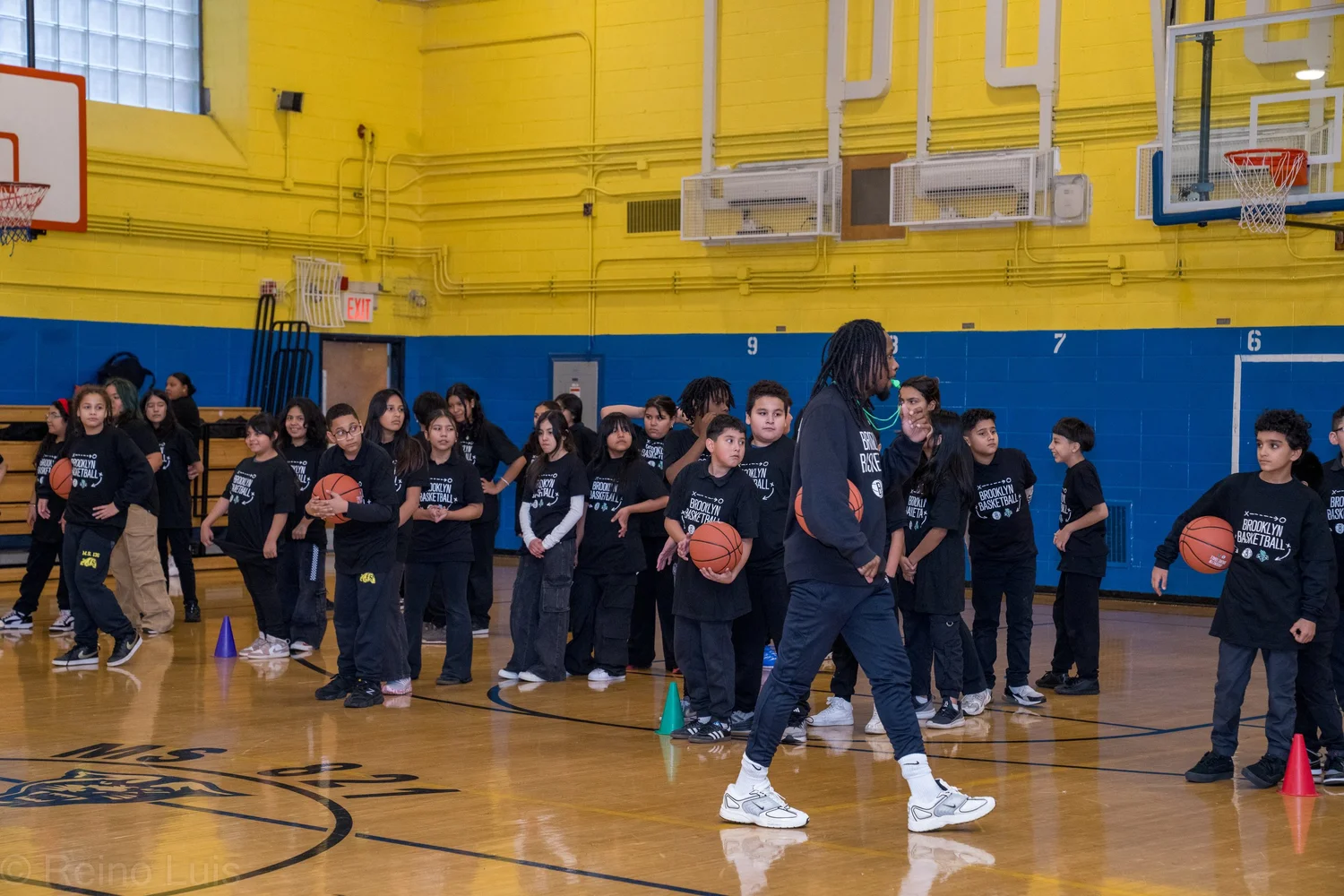 Students in Brooklyn Basketball shirts practice dribbling in school gymnasium