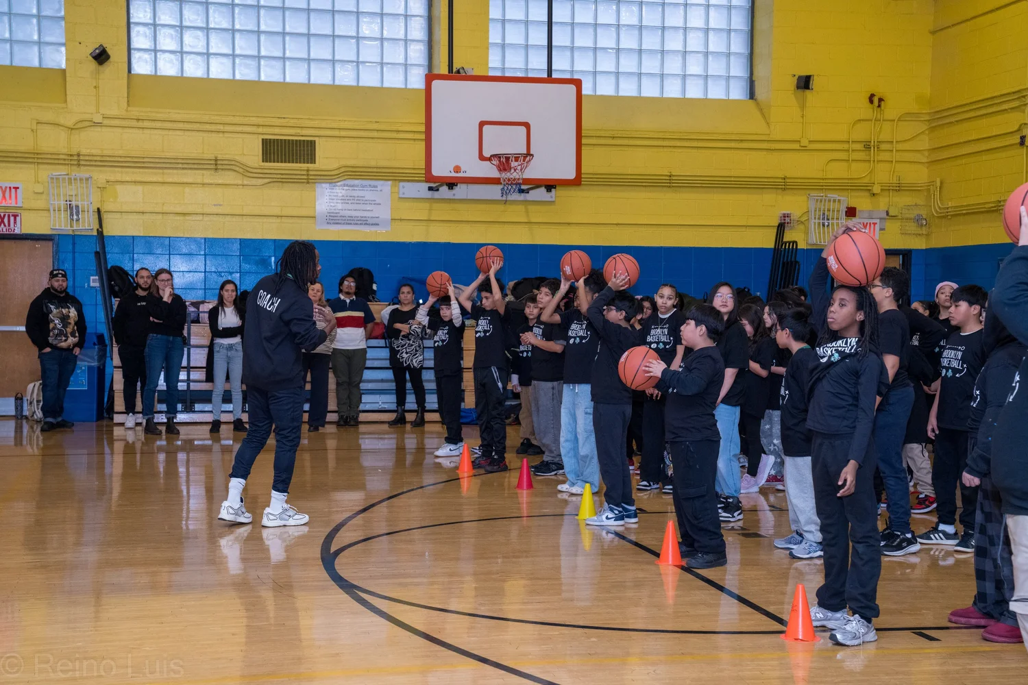 Students practice basketball drills with a coach in school gym