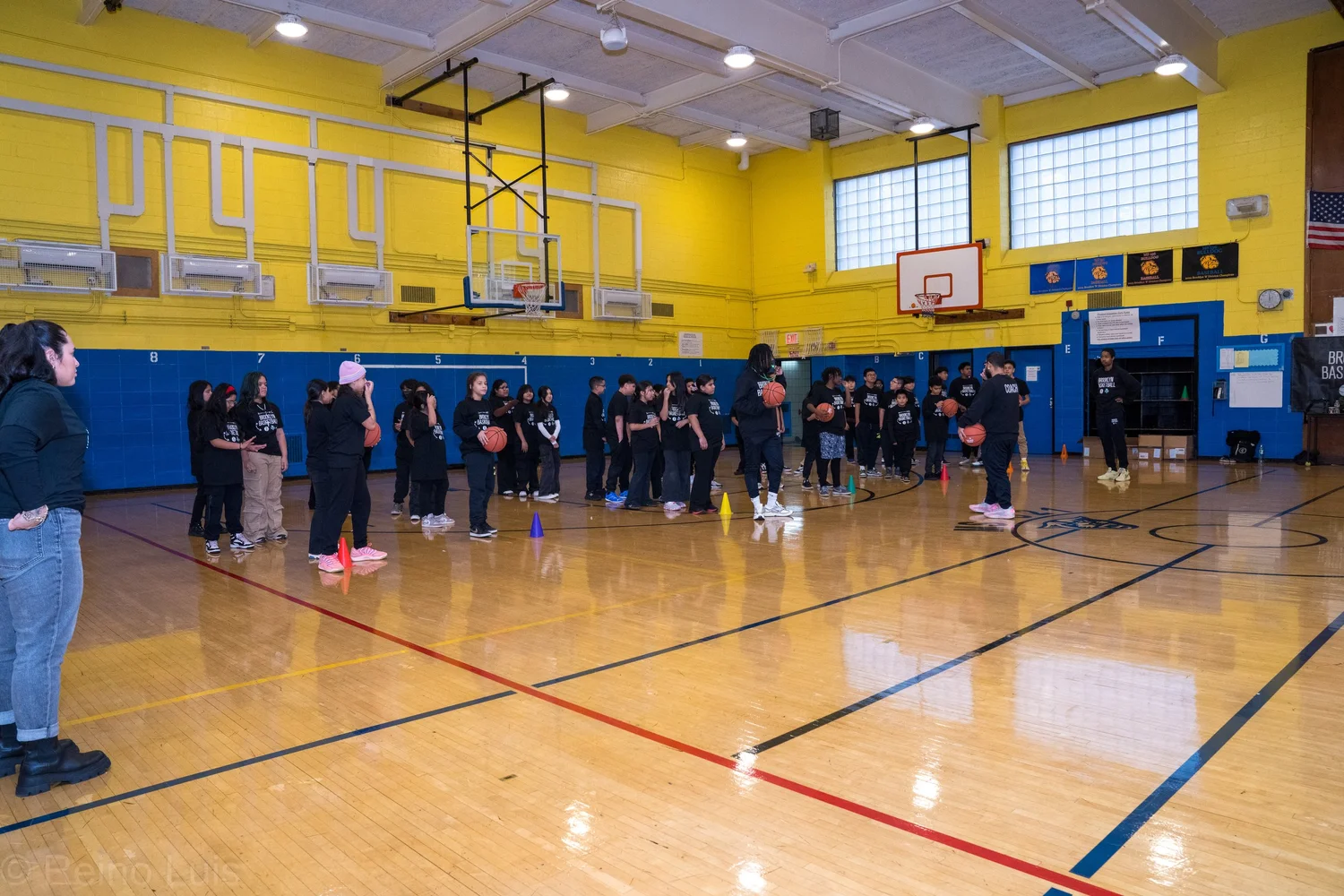 Students practicing basketball drills with cones in school gymnasium
