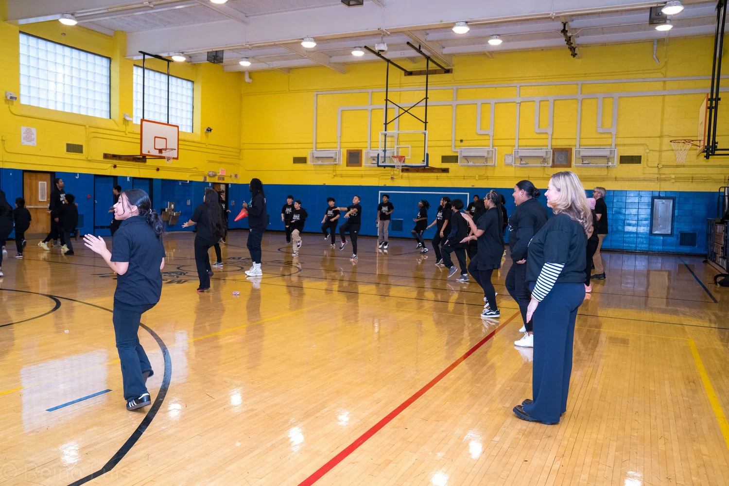 Students and adults rehearsing a dance routine in school gymnasium