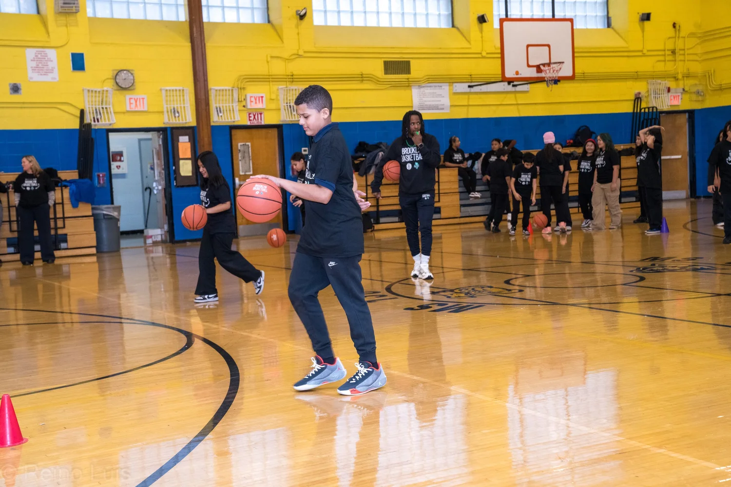 Students practicing basketball dribbling drills in school gymnasium