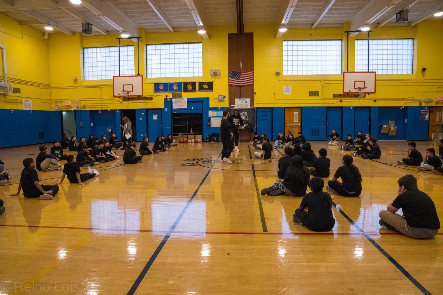 Students seated in gym circle listening to a speaker during assembly