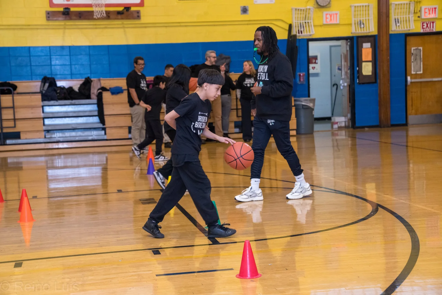 Student dribbling basketball through cones with adult coach supervising