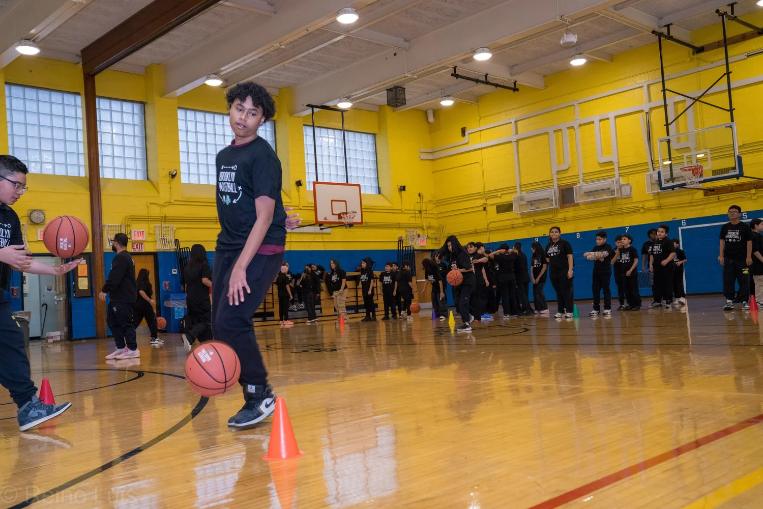 Students practicing basketball dribbling drills in school gymnasium