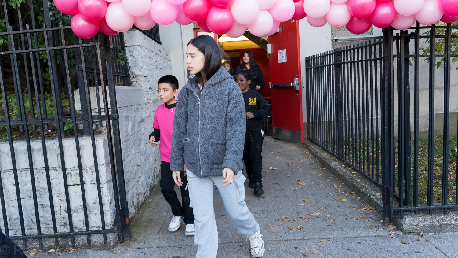 Students walking through school gate decorated with pink balloons