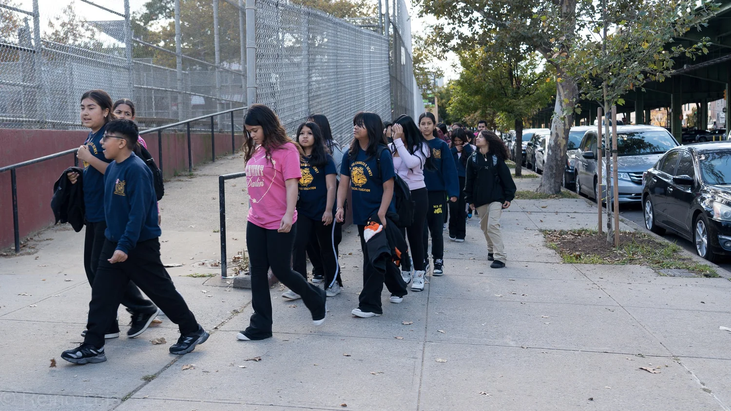Students walking in a line along a sidewalk outside school