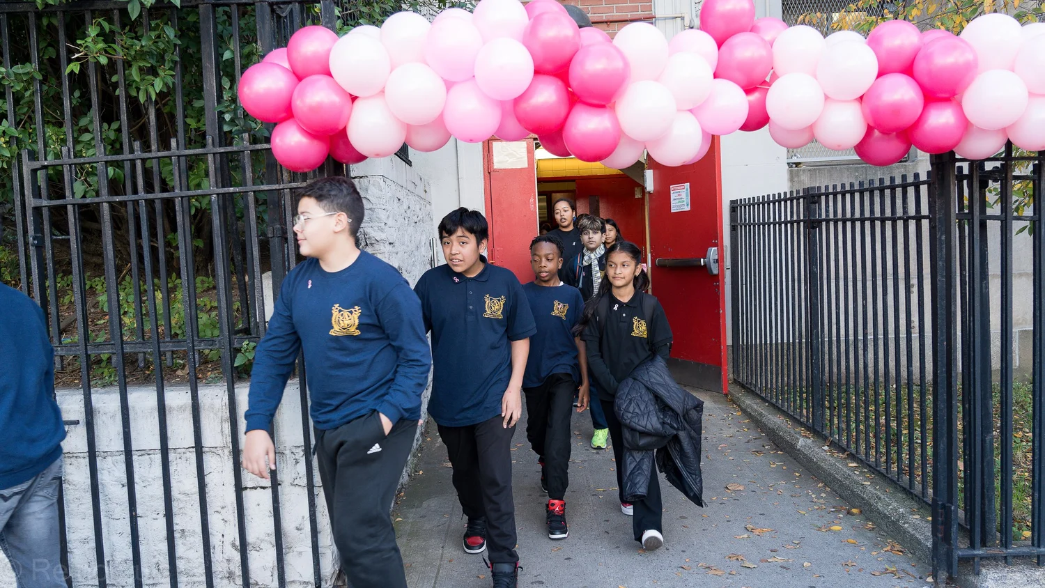 Students walking through school gate decorated with pink balloons