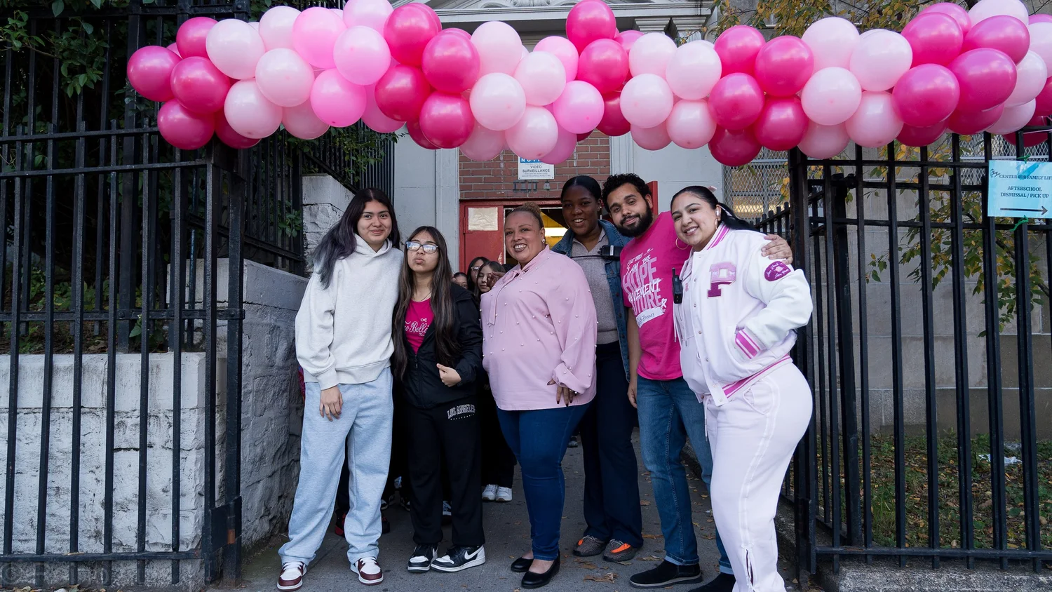 Students and staff posing under pink balloon arch at school entrance