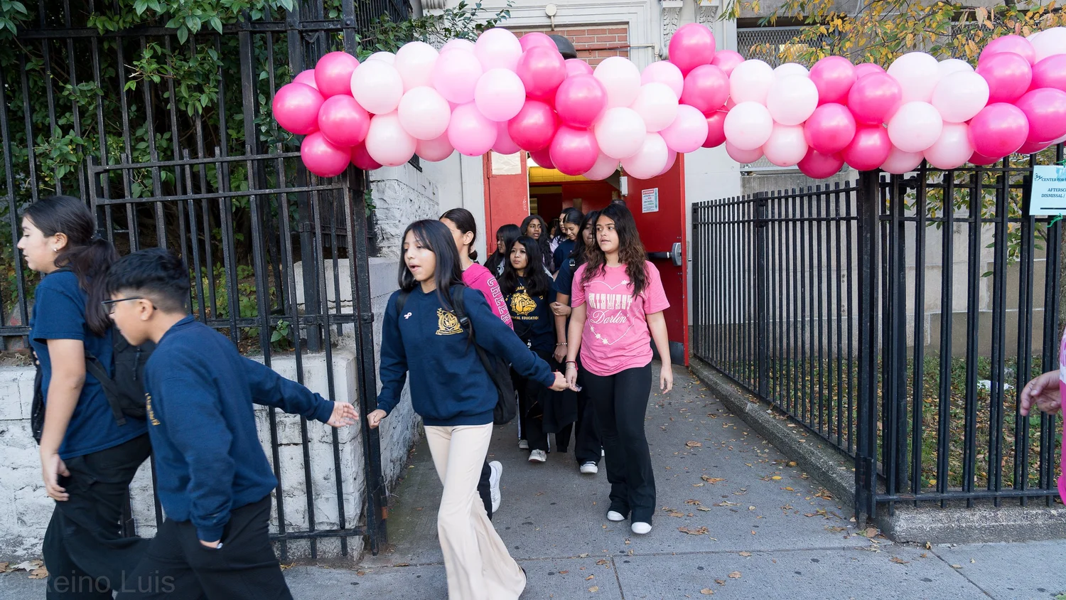 Students walking through gate under pink balloon arch at school event