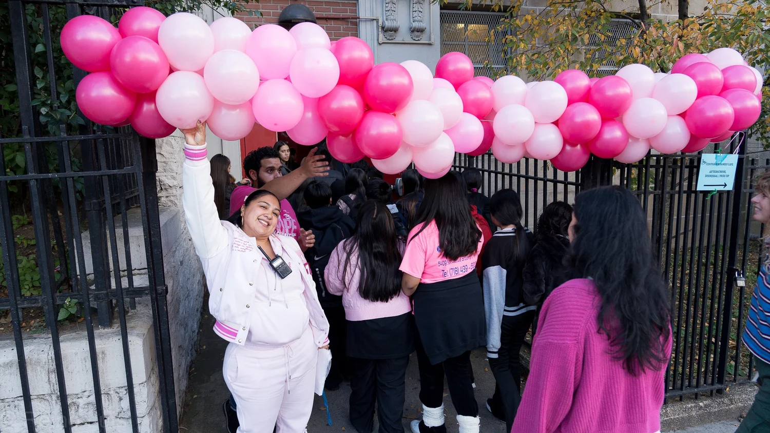 Students and staff celebrating under pink balloon arch at school entrance