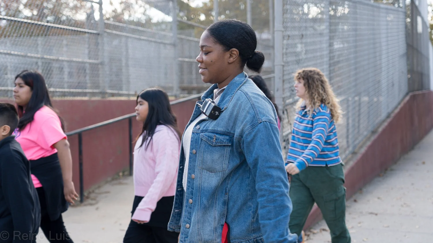 Students and staff walking outdoors along a fenced school pathway