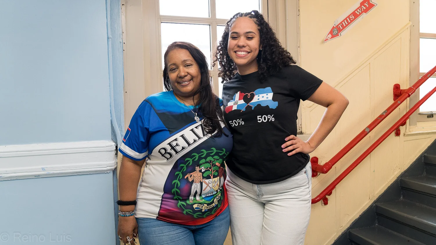 Two smiling women wearing cultural heritage shirts at school staircase