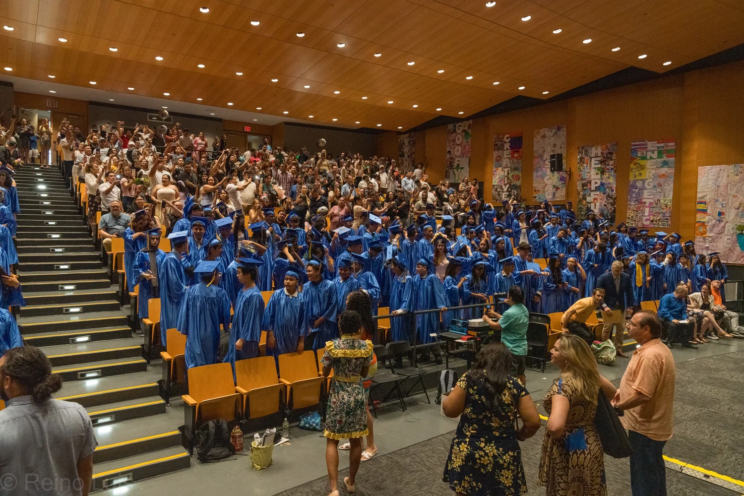 Students in blue caps and gowns celebrate at graduation ceremony