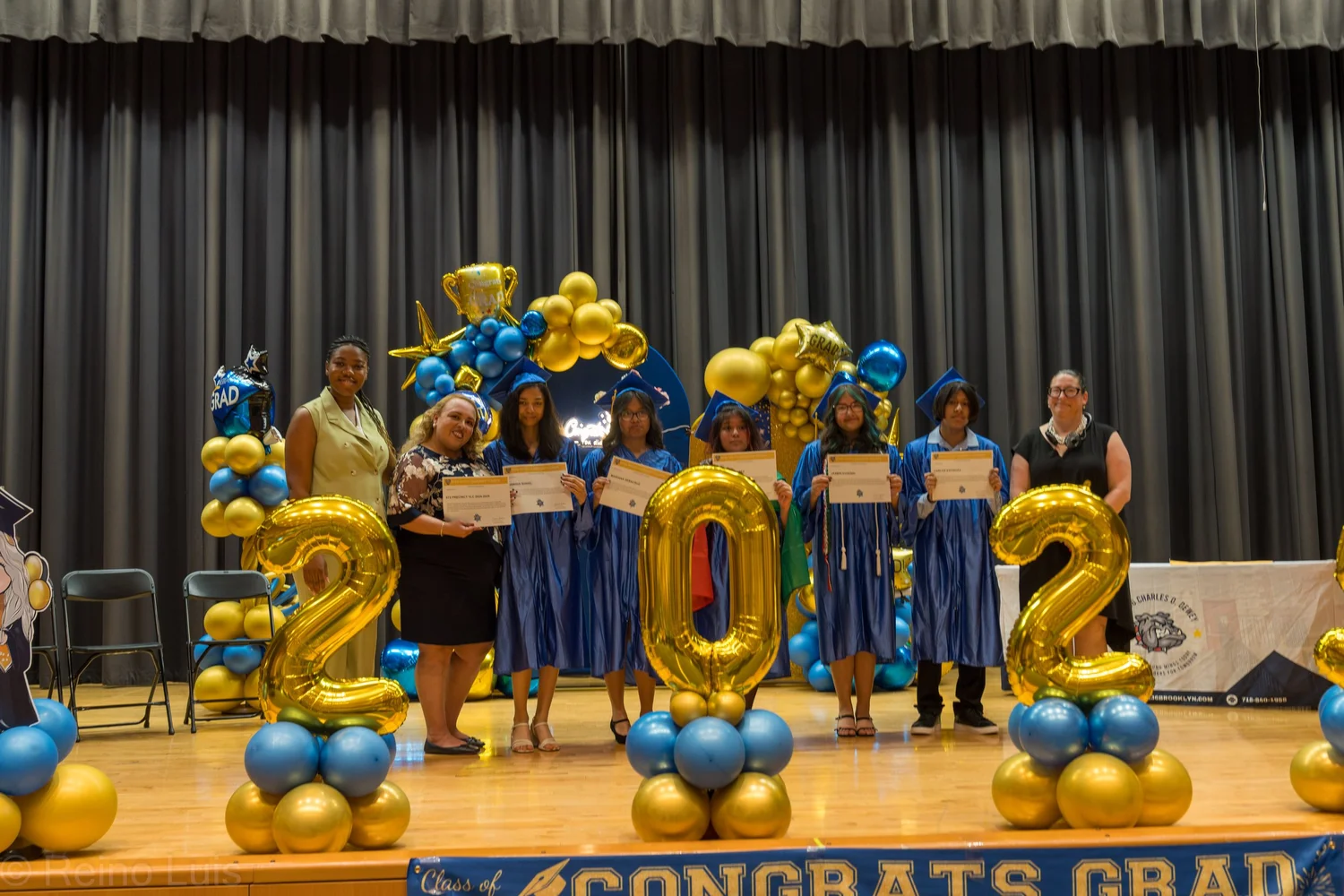 Students in blue caps and gowns holding diplomas on graduation stage