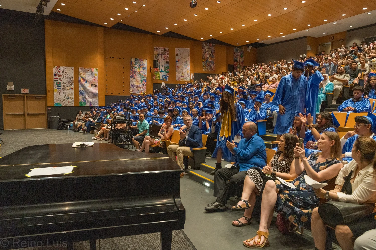 Students in blue caps and gowns fill auditorium during graduation ceremony