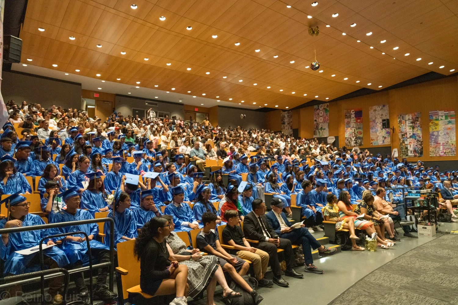 Students in blue cap and gown seated at graduation ceremony auditorium