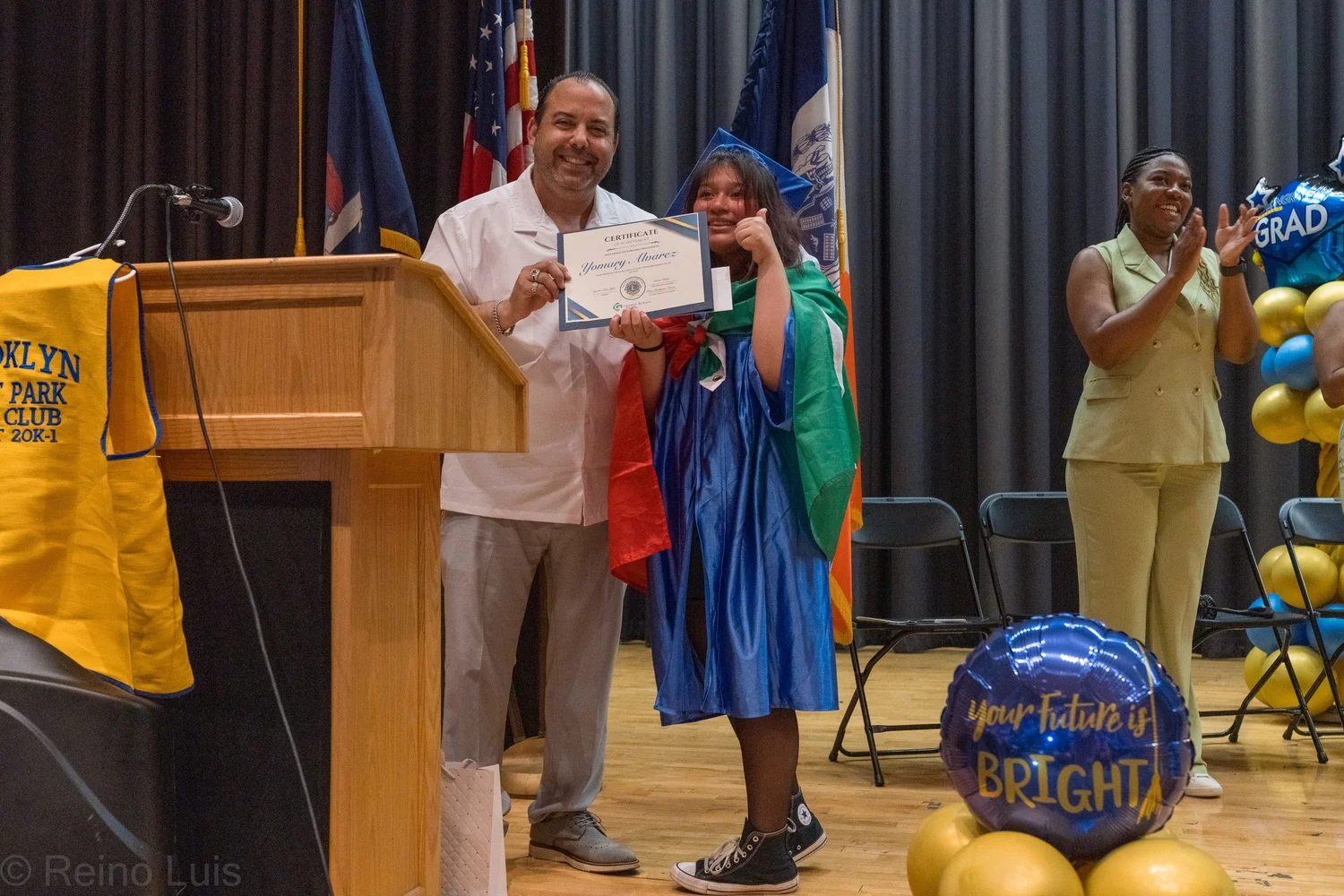 Student in blue graduation gown receives certificate on stage at ceremony