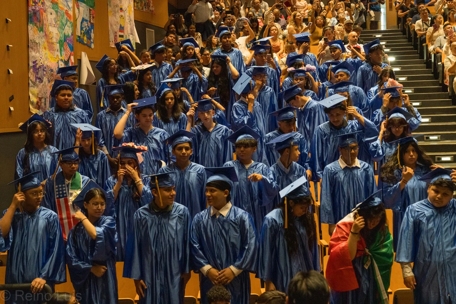 Students in blue caps and gowns during graduation ceremony in auditorium