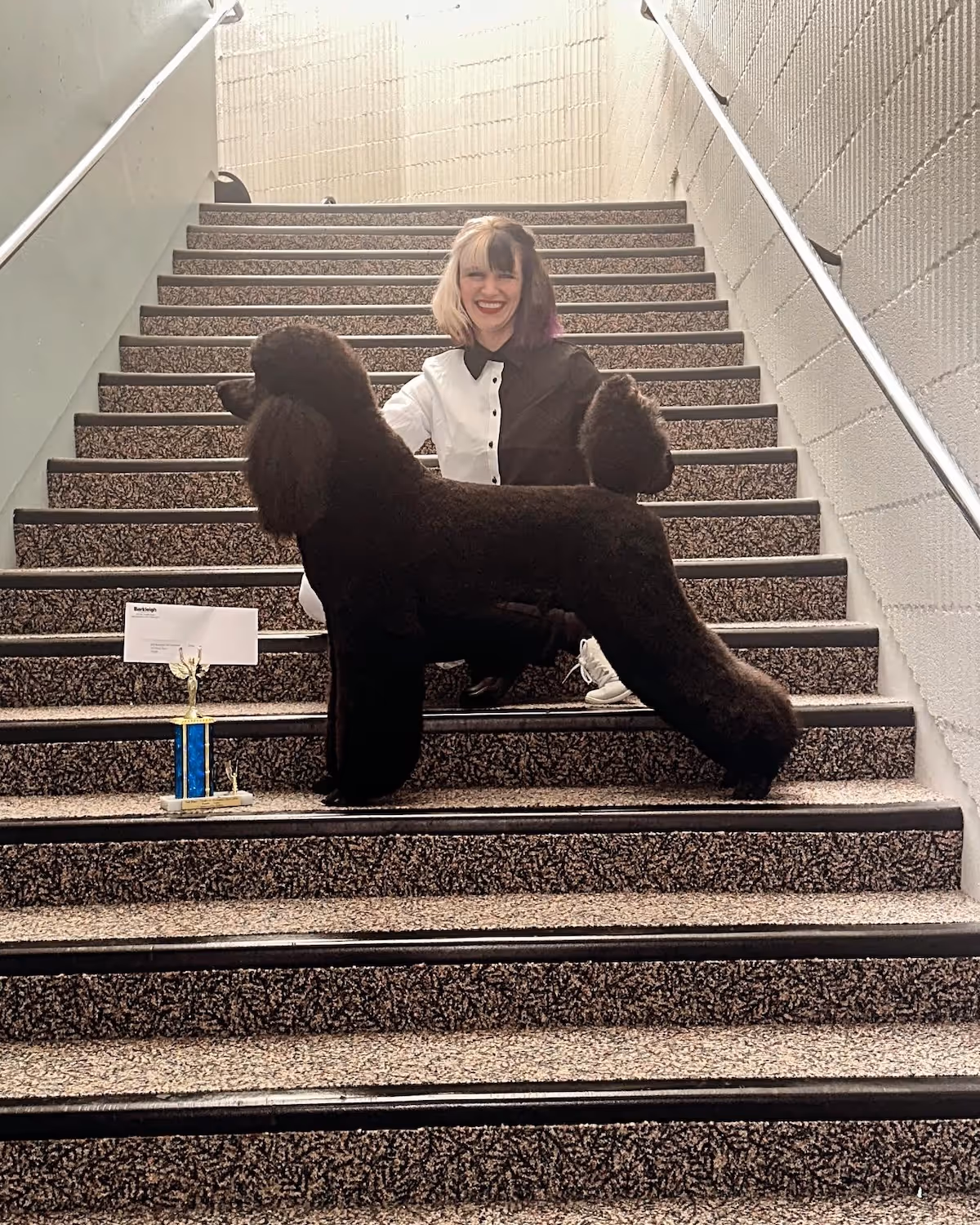 Constance Williams sitting on the stairs with a dog show trophy and poodle