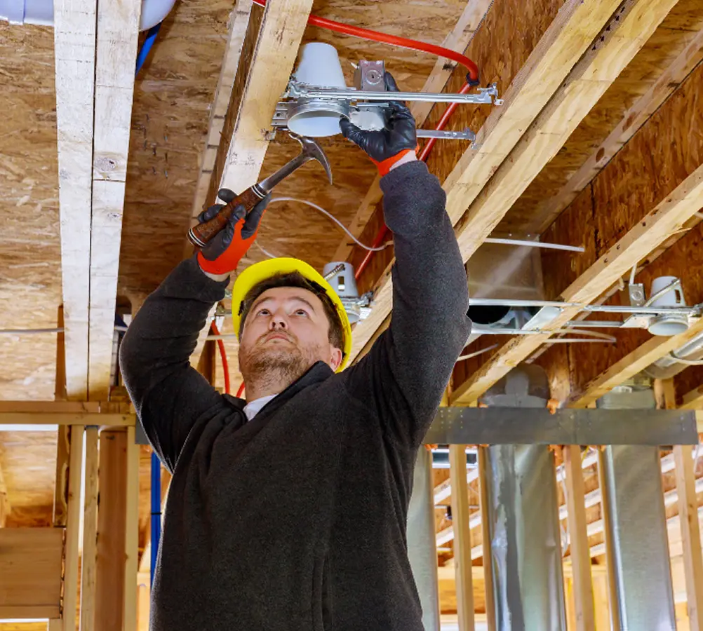 Electrician installing ceiling light fixture in building under construction.