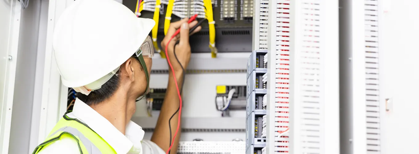 Electrician inspecting electrical panel with testing equipment. 