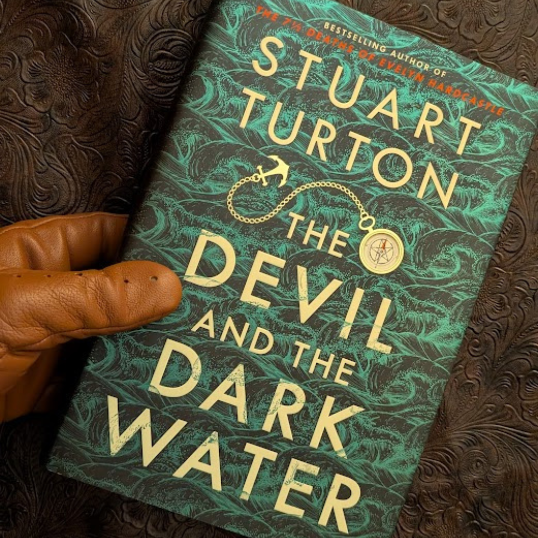 The curator's hand picking out "The Devil and the Dark Water" by Stuart Turton specifically for a reader