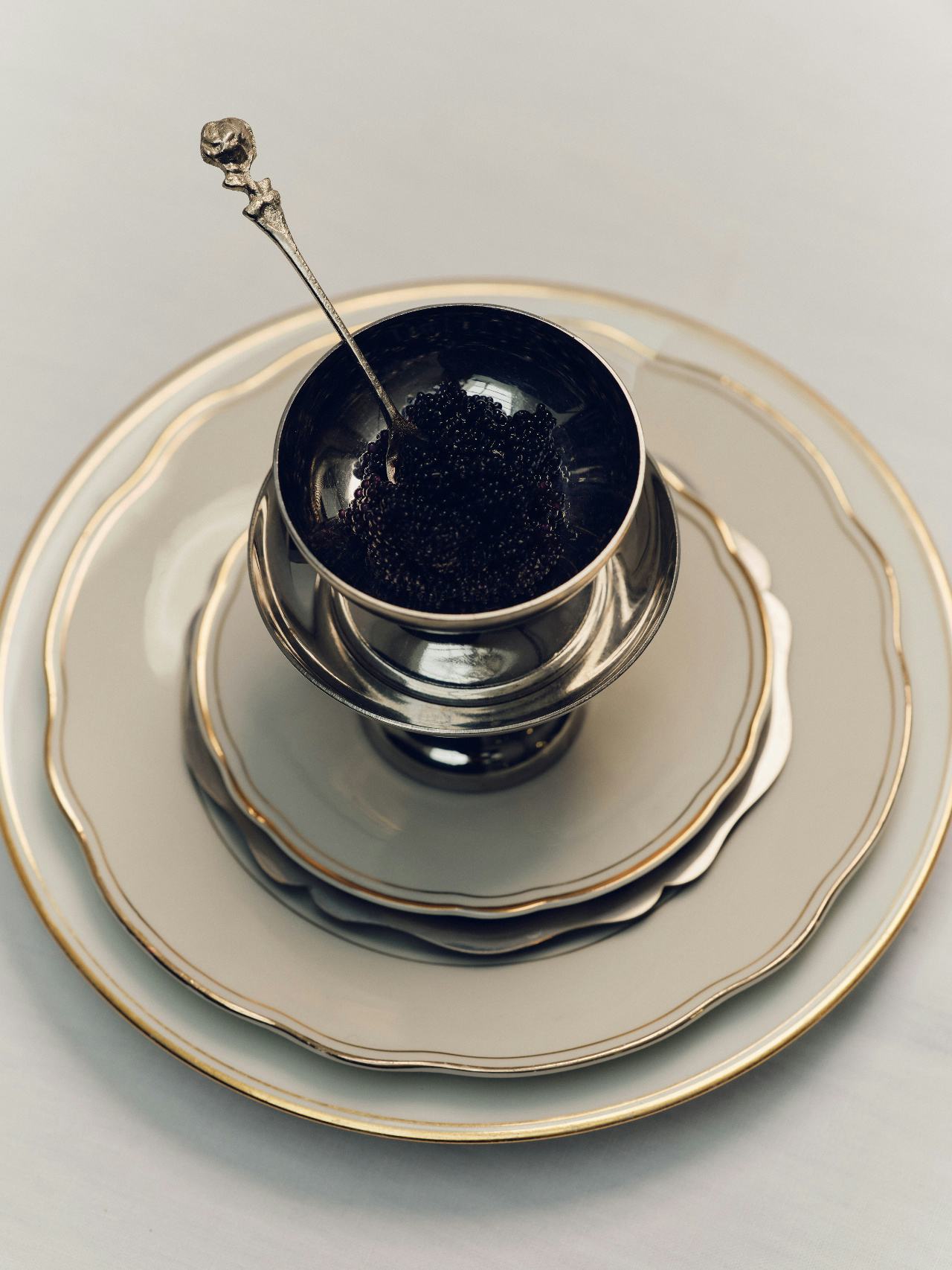 Three plates stacked with a silver bowl of Osetra Black Caviar and a silver spoon.