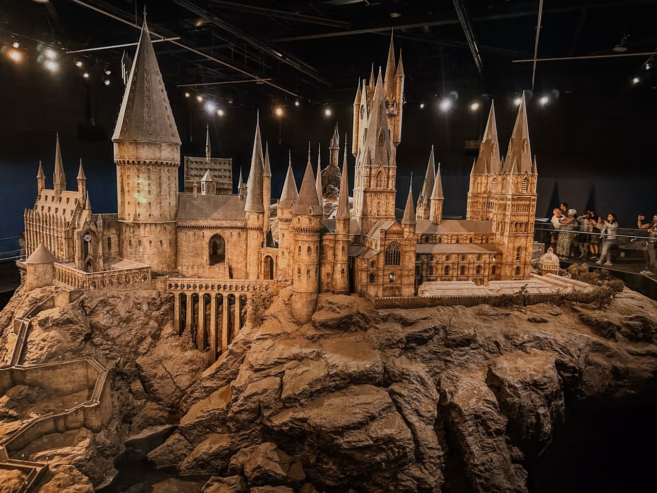 Detailed model of a large castle with tall spires and adjoining rocky cliff inside a museum.
