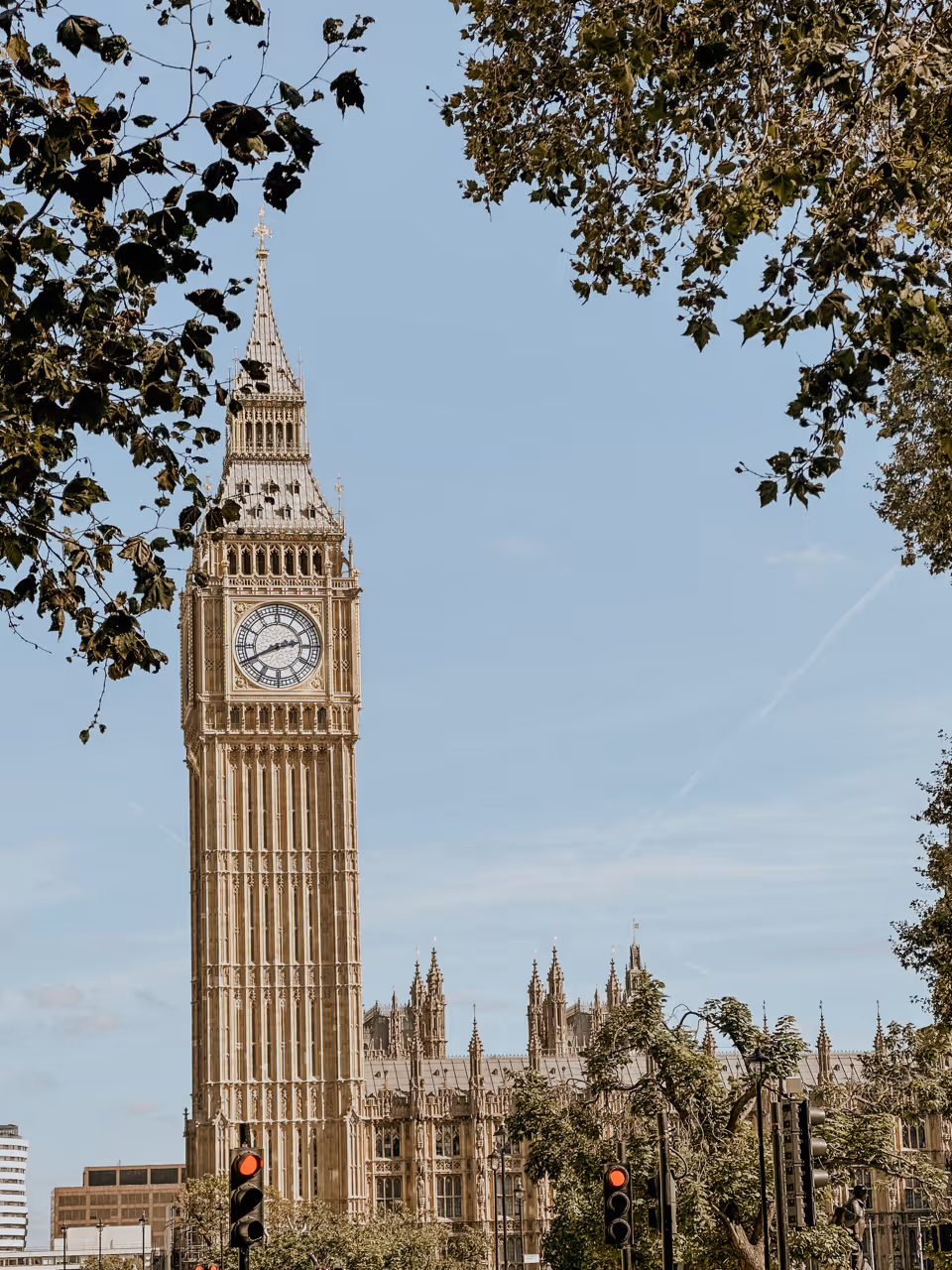 Big Ben clock tower in London framed by green tree leaves on a clear sunny day.