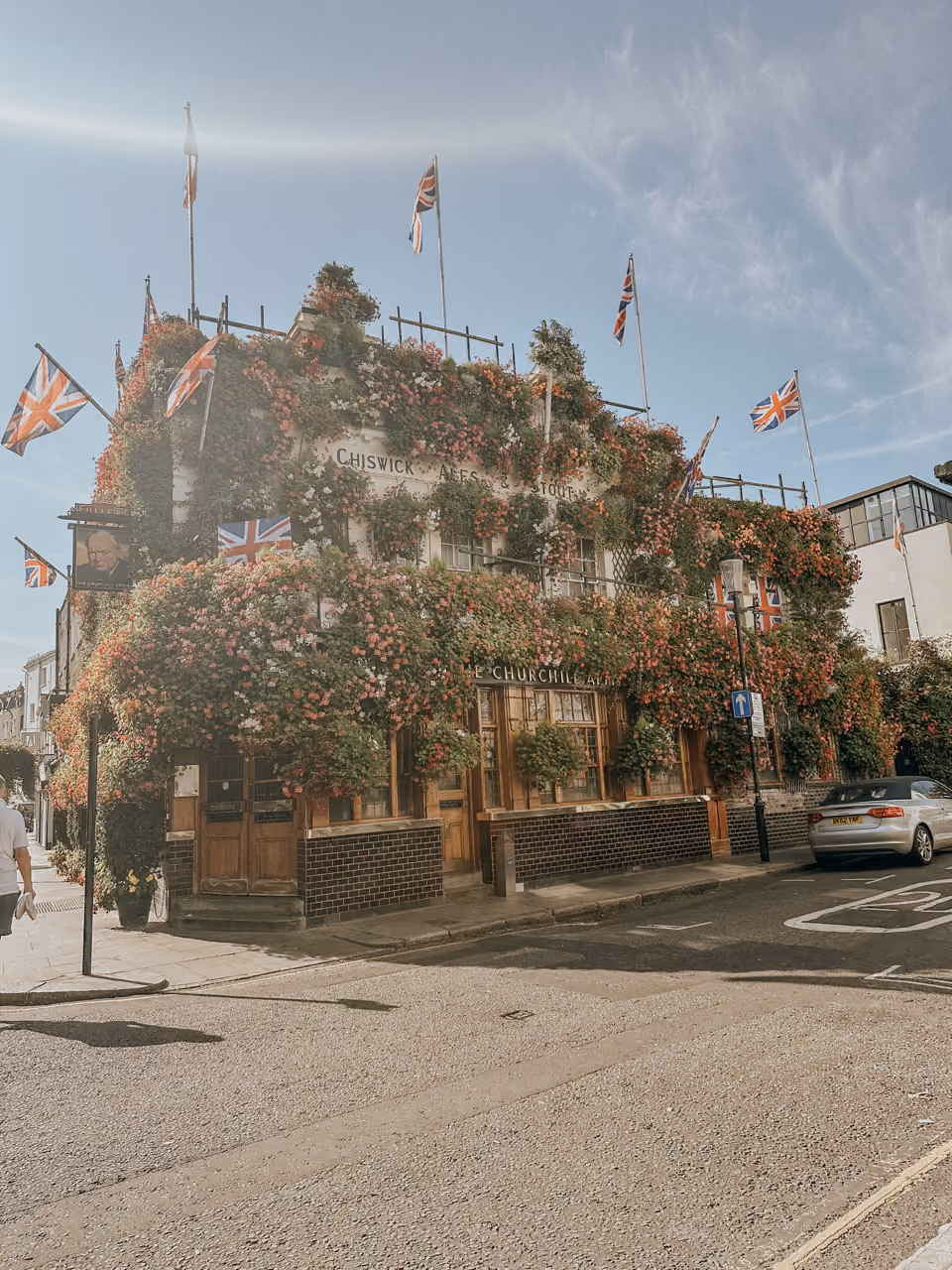 The Churchill Arms pub covered in flowers and UK flags on a sunny street corner.
