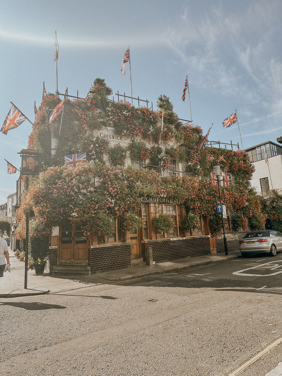 The Churchill Arms pub covered in flowers and UK flags on a sunny street corner.